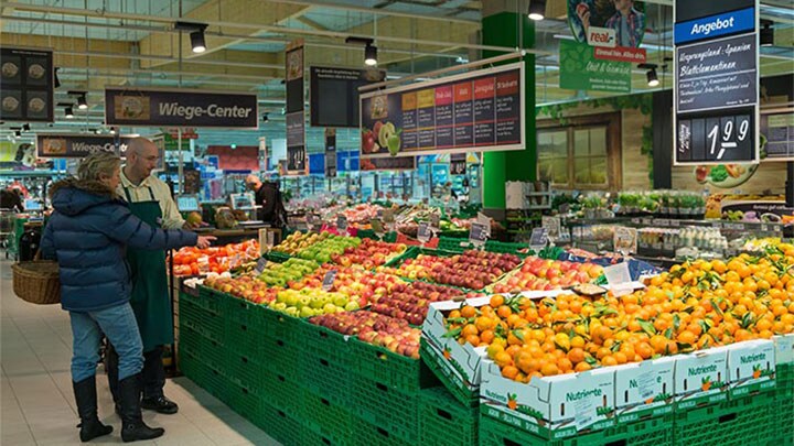 Customers look at fruits at Real which are illuminated using Philips supermarket lighting